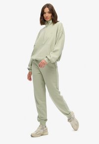 Lys grøn quarter-zip trøje med en frontlomme og matchende sweatpants i et blødt, tekstureret stof. Beige sneakers fuldender outfittet.