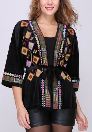 Veste kimono en velours noir ornée de broderies géométriques colorées, avec une taille à nouer et des manches larges. Les accents incluent des motifs dorés et roses.