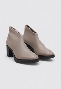 Beige Lederstiefeletten mit elegantem Design, spitzer Zehe und schwarzem Blockabsatz. Verfügt über sichtbare Nähte entlang des Schafts.