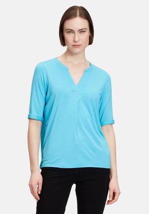 Top azzurro chiaro a maniche corte con scollatura a V e risvolti, caratterizzato da una sottile piega frontale e dettaglio del logo sotto la scollatura.