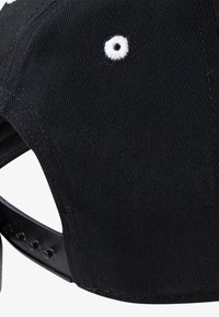 Sort baseball cap med struktureret stof, der har et hvidt ventilationshul og justerbar plastikrem med flere størrelsesnotcher.