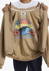 Light brown zippered jacket made from fabric with a soft texture, featuring a colorful graphic design of a wave and flowers on the front.
