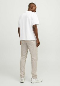 Camiseta de algodón blanca de manga corta, combinada con pantalones de lino beige claro y zapatillas blancas. Vista desde atrás, mostrando líneas limpias y ajuste.