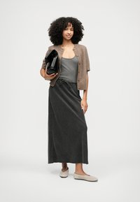 Gray maxi skirt with drawstring waist, paired with a gray tank top and a brown, short cardigan. Holding a black oversized bag.