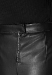 Jupe en cuir noir avec fermeture éclair, texture lisse et design ajusté. La taille est structurée pour un maintien sûr.