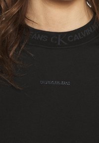 Černé tričko s kulatým výstřihem, s logem Calvin Klein Jeans v tmavě modré barvě na límci a tónovaným názvem značky na hrudi.
