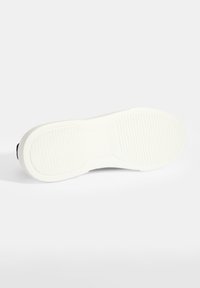 Weiße Gummisohle mit strukturiertem Grip-Muster. Abgerundete Zehen und flaches Profil mit subtiler Krümmung. Sauberes und minimalistisches Design.