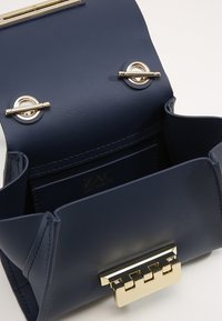 Marinblå läderhandväska med en lås i guld, har en rymlig insida och fickor för organisering. Enkel, strukturerad design.
