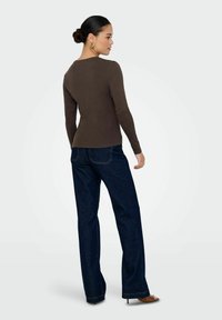 Maglietta marrone a maniche lunghe con scollatura rotonda, abbinata a jeans a gamba larga blu scuro, con dettagli di cucitura visibili e una superficie liscia.