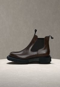 Botte Chelsea en cuir marron foncé avec des panneaux latéraux élastiques noirs et une semelle noire épaisse rainurée posée sur une surface claire avec un fond uni.