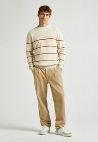 Kreminės megztos palaidinės su raudonomis juostelėmis, derinamos su smėlio spalvos klostuotomis kelnėmis. Avalynė - baltos sportbačiai. Paprastas, kasdieniškas dizainas.