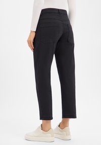 Pantalon noir à taille haute, coupe droite, avec deux poches arrière. Porté avec des baskets blanches, affichant une finition soignée.