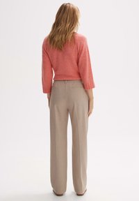 Pull rose clair en maille lâche avec manches 3/4, associé à un pantalon beige taille haute, présentant une coupe droite et des poches arrière.