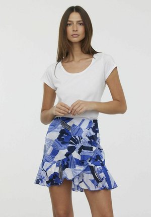 Haut blanc à manches courtes associé à une jupe bleue à motifs avec volants, motifs floraux et textures alternées dans différentes nuances de bleu.