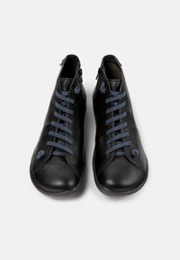 Botas de tobillo de cuero negro con una textura suave, con cordones azules, cierre con cremallera y punta redonda. Diseño limpio con un minimalismo en los detalles.