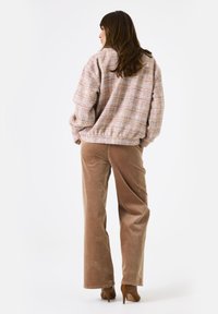 Roze en multikleurige gestructureerde oversized jas met geribbelde zoom, gecombineerd met hoog aangesloten beige ribfluwelen broek en bruine hakken.