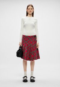 Un haut blanc à manches longues, une jupe à carreaux rouges avec des lignes vertes, un sac à main noir, des chaussettes blanches et des chaussures noires avec des boucles. Textures plates et lisses.