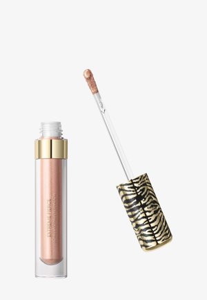 Ombre à paupières liquide dans un tube transparent avec un bouchon doré, applicateur avec une ombre beige scintillante et un manche rayé zèbre noir et or.