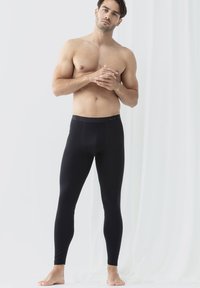 Zwarte legging van rekbaar materiaal met een gladde textuur en een elastische tailleband, aansluitend om de benen, gedragen op blote voeten.
