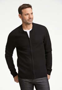 Mustavälinen vetoketjullinen kardigan, jossa on ribattuja kaulus ja hihansuut. Se on valmistettu sileästä kankaasta, ja siinä on muotoiltu leikkaus sekä yksinkertainen pinta.