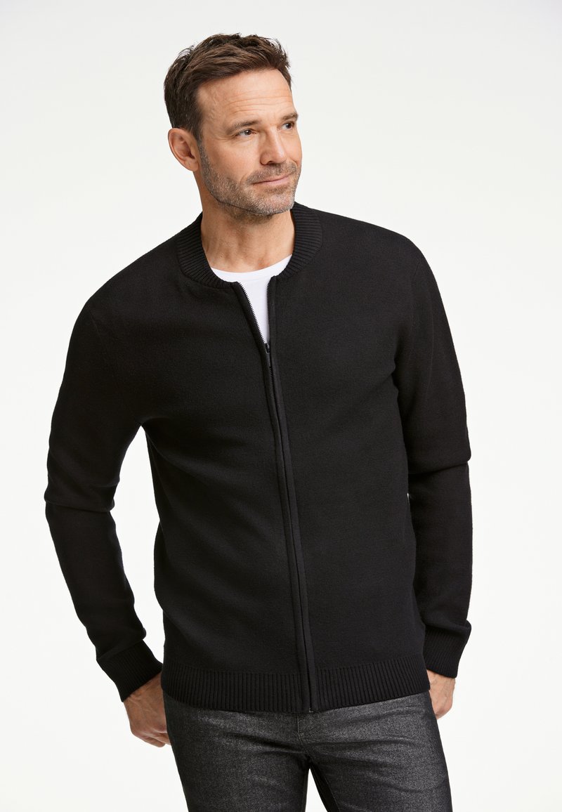 Mustavälinen vetoketjullinen kardigan, jossa on ribattuja kaulus ja hihansuut. Se on valmistettu sileästä kankaasta, ja siinä on muotoiltu leikkaus sekä yksinkertainen pinta.