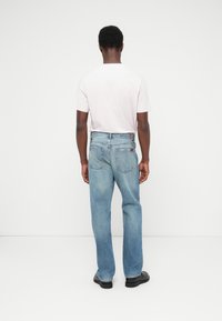 Világoskék, egyenes szárú farmernadrág, hátul zsebekkel és enyhén kopott hatású felülettel. Egyszerű fehér inggel párosítva.