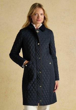 Marineblauer gesteppter Mantel mit Rautenmuster, Stehkragen, Druckknopfverschlüssen und zwei Fronttaschen. Mit goldfarbener Hardware akzentuiert.