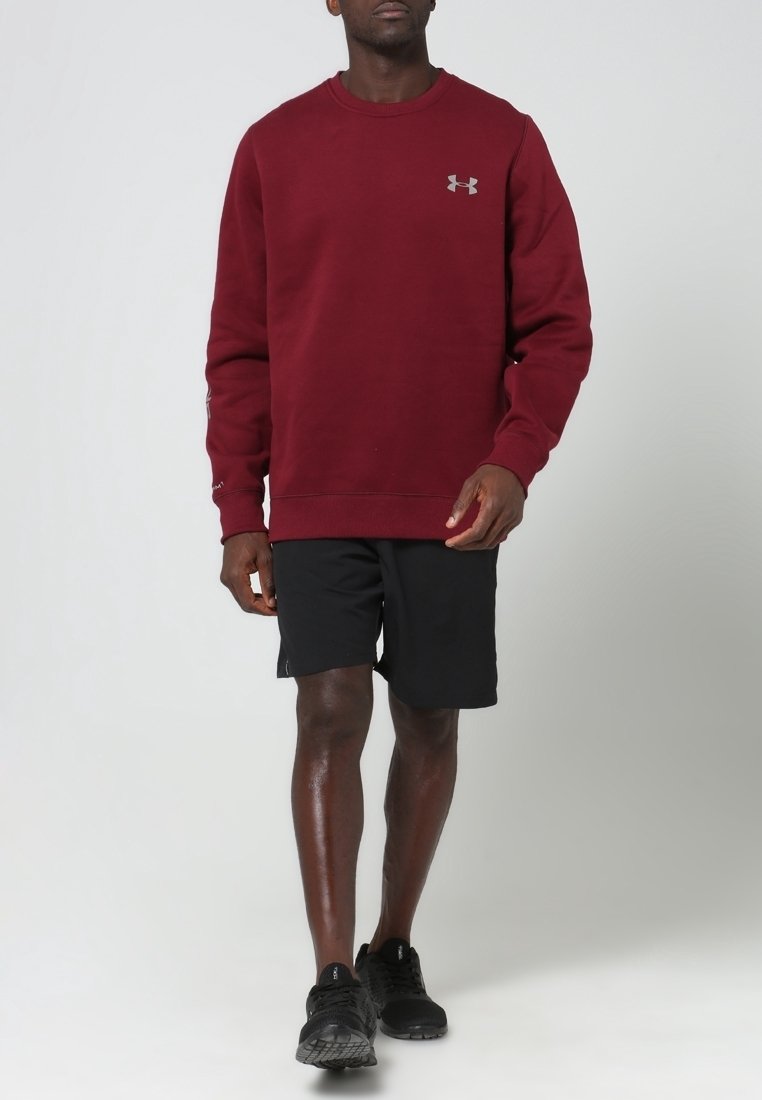 Sweatshirt bordeaux à manches longues et col rond, associé à un short noir et des chaussures de sport noires, avec un logo sous l'aisselle.