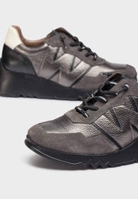 Zapatillas gris con una mezcla de texturas mate y brillantes, con un diseño de capas, cordones negros y una suela de goma gruesa.