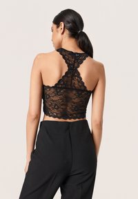 Top corto de encaje negro con dobladillo festoneado y diseño de espalda nadadora, combinado con pantalones negros de cintura alta.