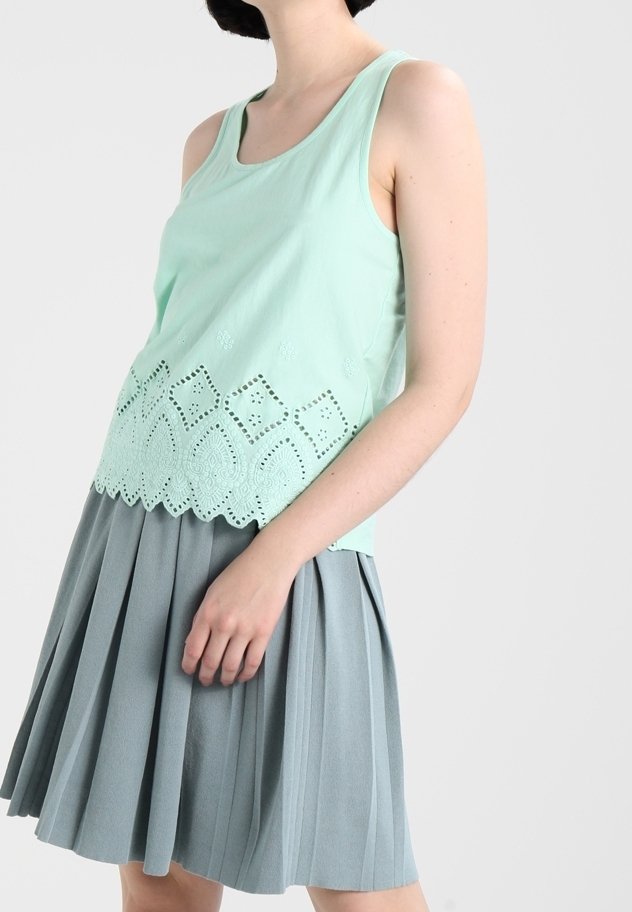 Mintgrön linne med spetsdetaljer vid nederkanten, kombinerat med en grå plisserad kjol. Tygerna ser mjuka och lätta ut.