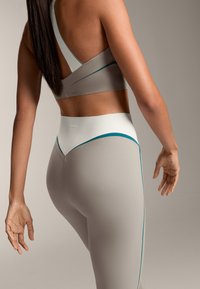 Set športnega modrčka in leggingov v svetlo sivi barvi z teal poudarki. Modrček ima dizajn s križnim hrbtom, medtem ko imajo leggings visok pas.