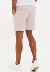 Shorts rosa chiaro realizzati in tessuto, con tasche laterali e posteriori, caratterizzati da un design pulito e un orlo dritto. Abbinati a sneakers bianche.