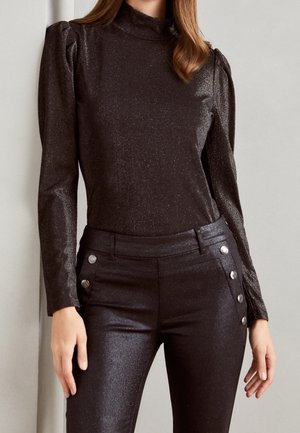 Schwarzes, langärmliges Oberteil mit hohem Kragen und puffigen Schultern aus einem glänzenden, strukturierten Stoff. Dazu passende, taillierte Hose mit silbernen Knöpfen.