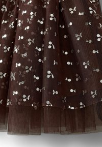 Țesătură din tull maro cu un design stratificat, având modele cu cireșe și frunze din folie argintie pe tot parcursul. Textură moale cu un finisaj semi-transparent.