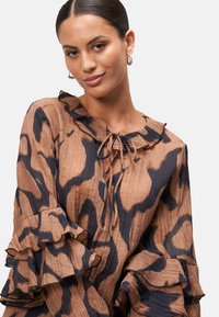 Brown animal print blouse featuring ruffled sleeves, a tie neck, and textured fabric with an irregular pattern.