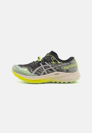 Zapatilla de trail running con un upper en patrón negro y verde, entresuela gris y acentos en amarillo brillante. Presenta una suela texturizada para mayor agarre.