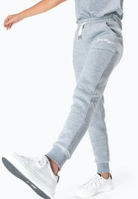Grijze sweatpants met elastische tailleband, zijzakken, aangesloten enkels en witte logodetails op de linkerdij, gecombineerd met witte sneakers.