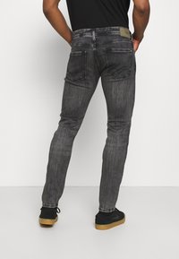 Slim-fit šedé džíny vyrobené z denimu, s zadními kapsami se švy a logem na pásku, doplněné černými teniskami.