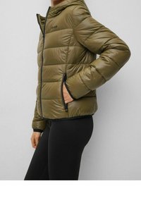 Giacca imbottita verde oliva con cappuccio, zip frontale e due tasche laterali. Presenta un'imbottitura orizzontale e dettagli neri attorno alle zip.