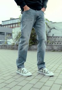 Jeans azules desgastados de corte recto, con textura usada, combinados con zapatillas de lona a rayas blancas y negras con suelas blancas.