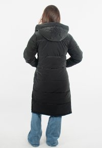 Manteau matelassé noir avec capuche, de longueur longue, au design matelassé et à la finition texturée. Associé à un jean évasé bleu.