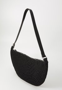 Borsa nera intrecciata con forma curva, superficie testurizzata, chiusura con zip e tracolla piatta in pelle attaccata con accessori in metallo argentato.