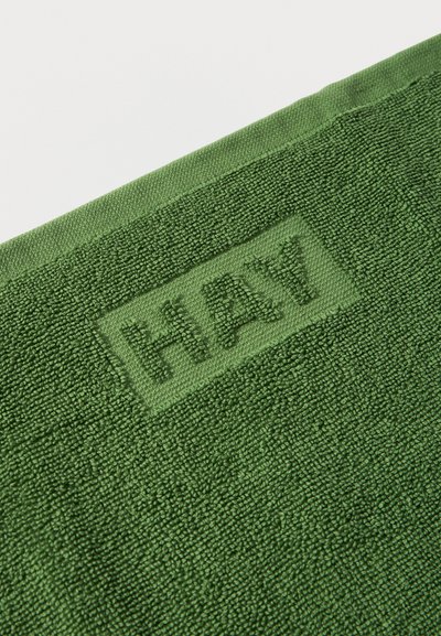 Σκούρο πράσινο υφασμάτινο με υφή, με την λέξη "HAY" ανάγλυφα κοντά στην άκρη, δείχνοντας μια κοντινή εικόνα του υφαντού υλικού και της ραφής.