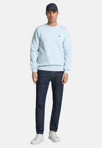 Sudadera azul claro, con cuello redondo, con logo; jeans oscuros; zapatillas blancas; ajuste casual; textura suave; mangas cortas, debajo de la sudadera.