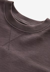Hnedý crewneck sveter s rebrovaným výstrihom, so subtílnym krížovým šthetom a mäkkou textúrou látky. Nastaviteľný a pohodlný dizajn.