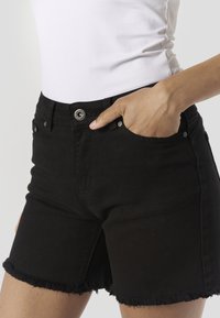 Pantalones cortos de mezclilla negra con dobladillo deshilachado, cinco bolsillos y cierre de botón plateado. Fabricados con tela resistente, con un diseño ajustado.