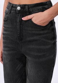 Svarte denimjeans med høy midje, med en frontlomme, subtile falminger og en sølvknapplukking for ekstra detaljer.