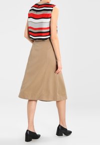 Ingekort gestreept topje in rood, zwart, grijs en wit, gecombineerd met een beige A-lijn rok en zwarte block-heeled schoenen.