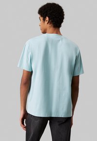 Jasnoniebieska koszulka z krótkim rękawem wykonana z bawełny. Okrągły dekolt i luźny krój, o gładkiej fakturze i prostym designie. Do niej noszone ciemne dżinsy.